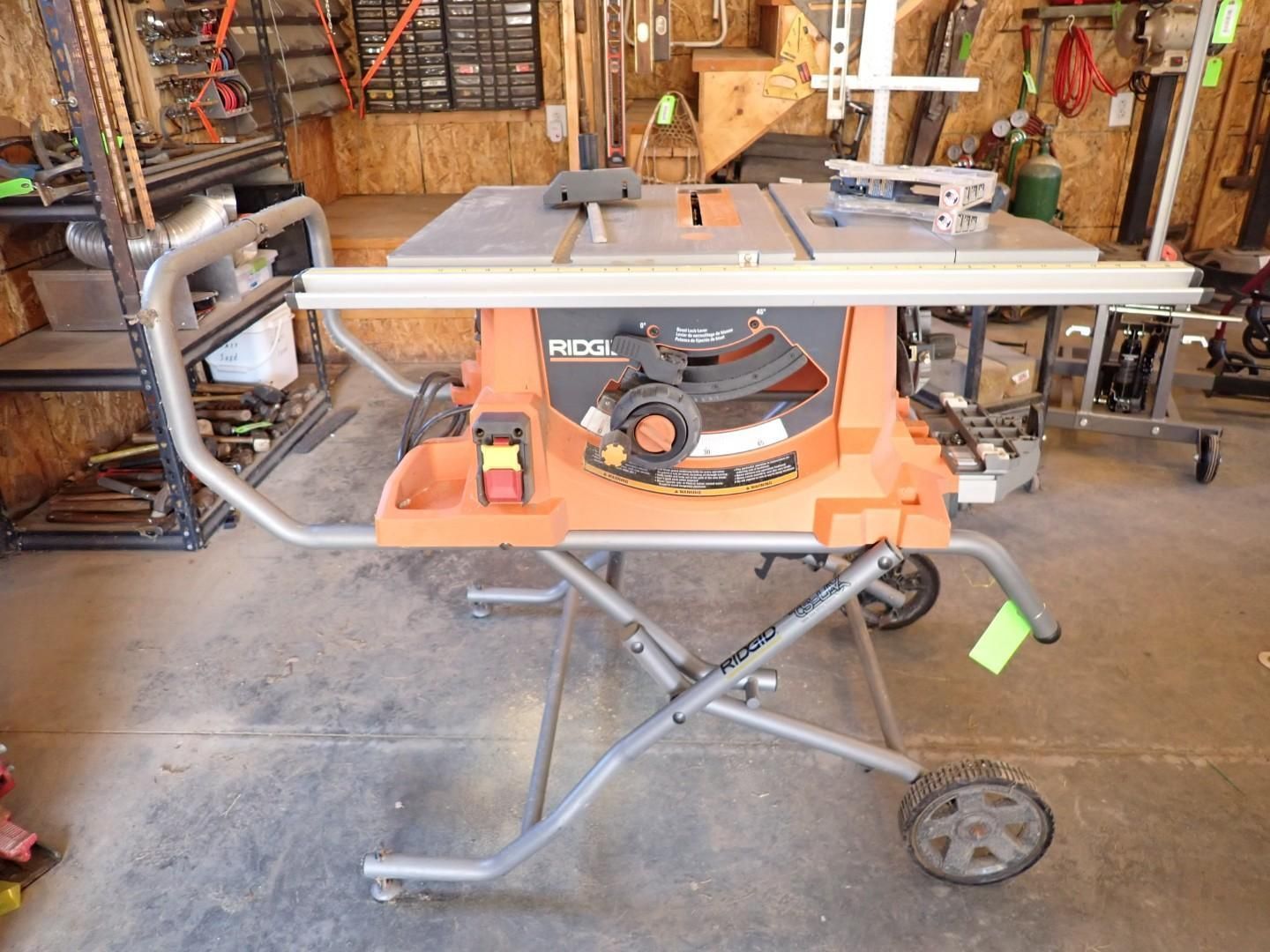 Orange Ridgid table saw on a wheeled stand in a workshop garage, with tools and wood in the background
