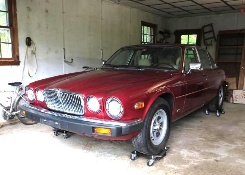 Red Jaguar sedan on wheel dollies in a garage.