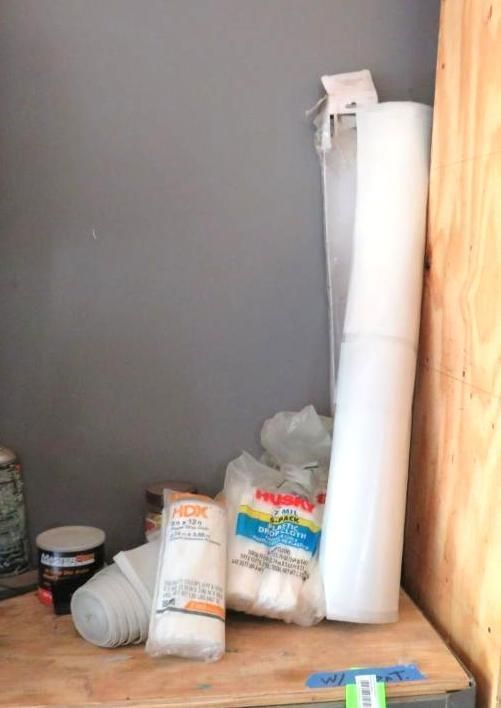 Rolls of clear plastic wrap and bags of packing supplies on a wooden shelf.