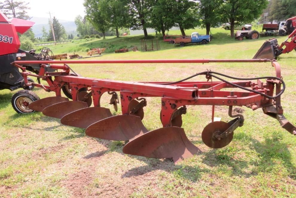 Red plow attached to tractor in a grassy field.