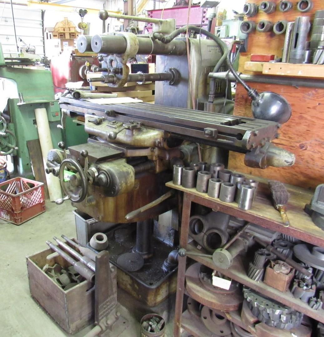 An old industrial milling machine in a workshop with assorted parts and tools.