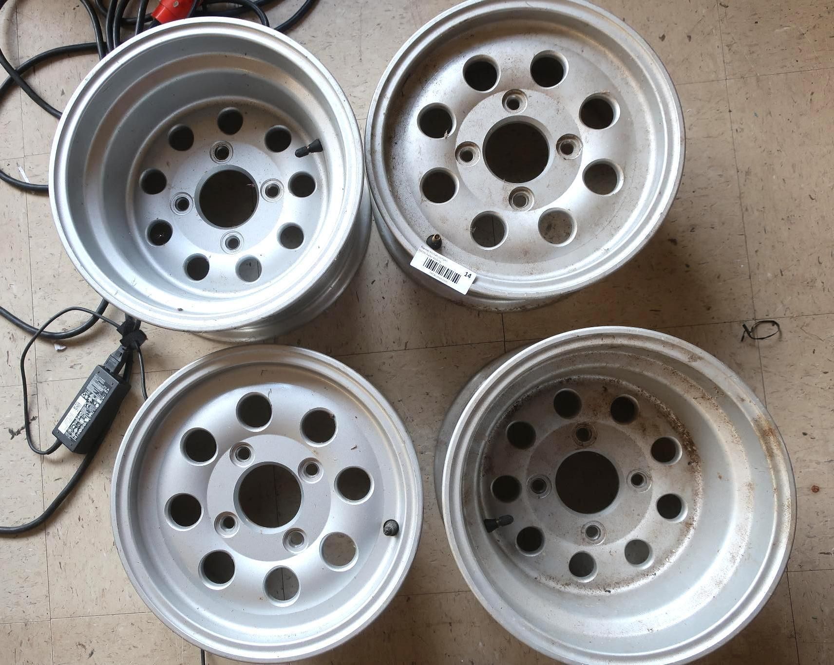 Four silver alloy wheels with multiple circular holes, sitting on a floor.