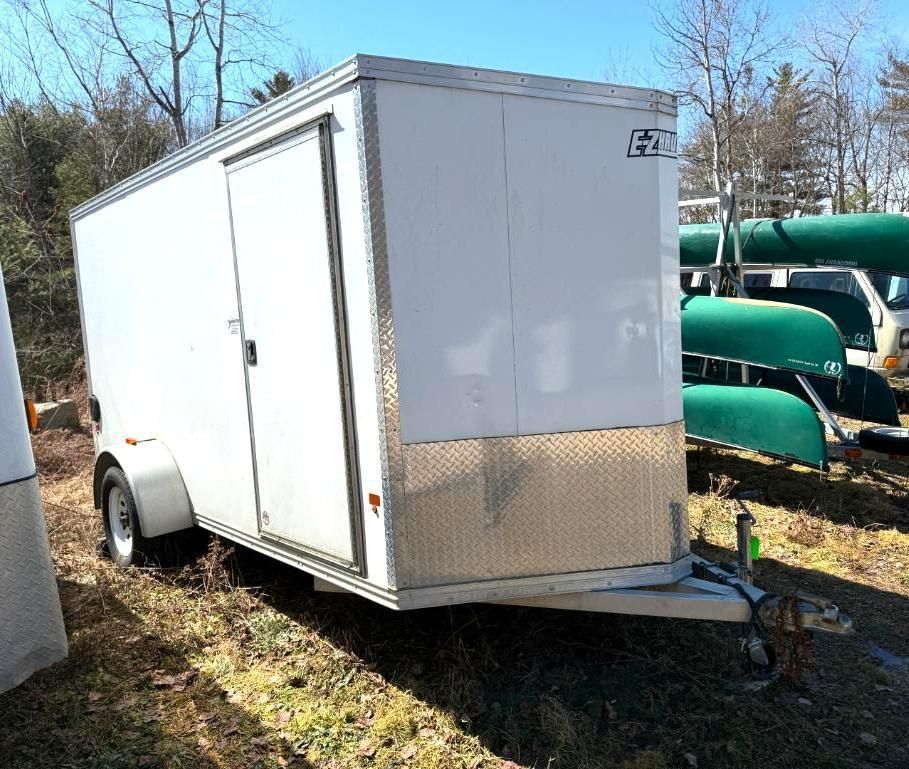 White enclosed cargo trailer with a diamond plate bottom, parked outside.