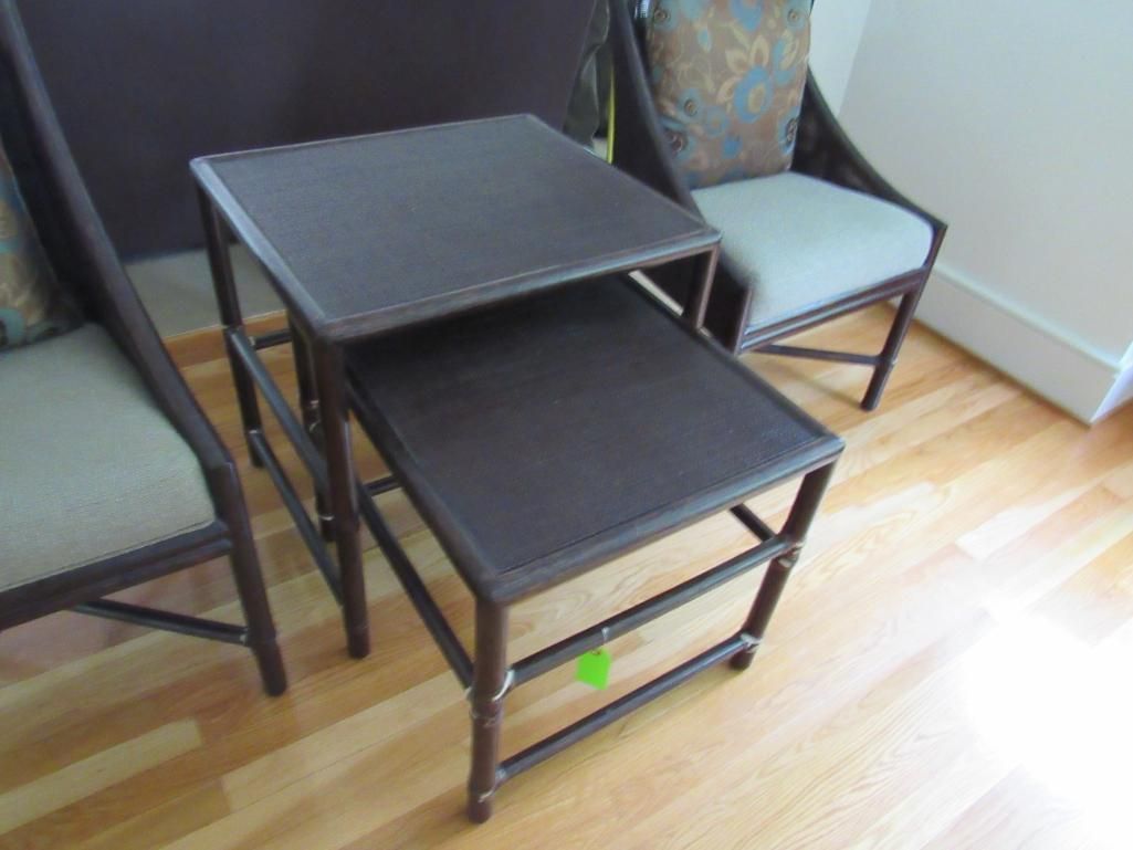 Two dark brown nesting tables next to upholstered chairs on a light wood floor.