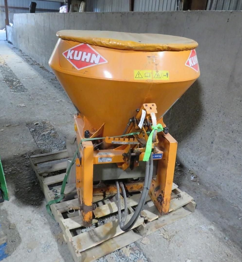 Orange Kuhn fertilizer spreader on a wooden pallet in a shed.