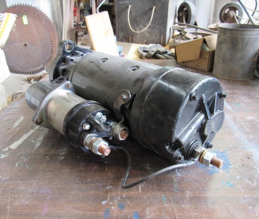 Black and silver electric motor on a wooden surface, with copper connectors and wires.