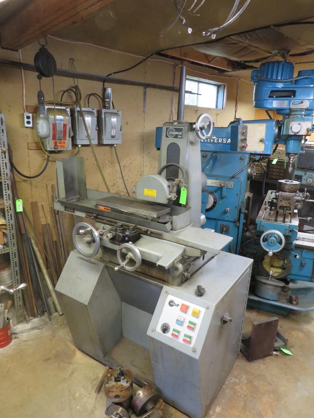 A gray industrial surface grinder machine with control panel and grinding wheel. In a workshop setting.