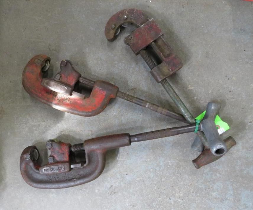 Three pipe cutters on a gray surface, angled towards each other.