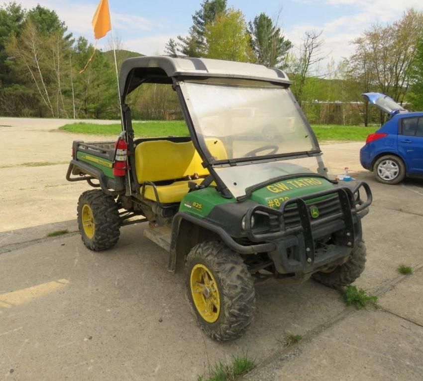 John Deere Gator utility vehicle with a windshield and orange safety flag parked outdoors.