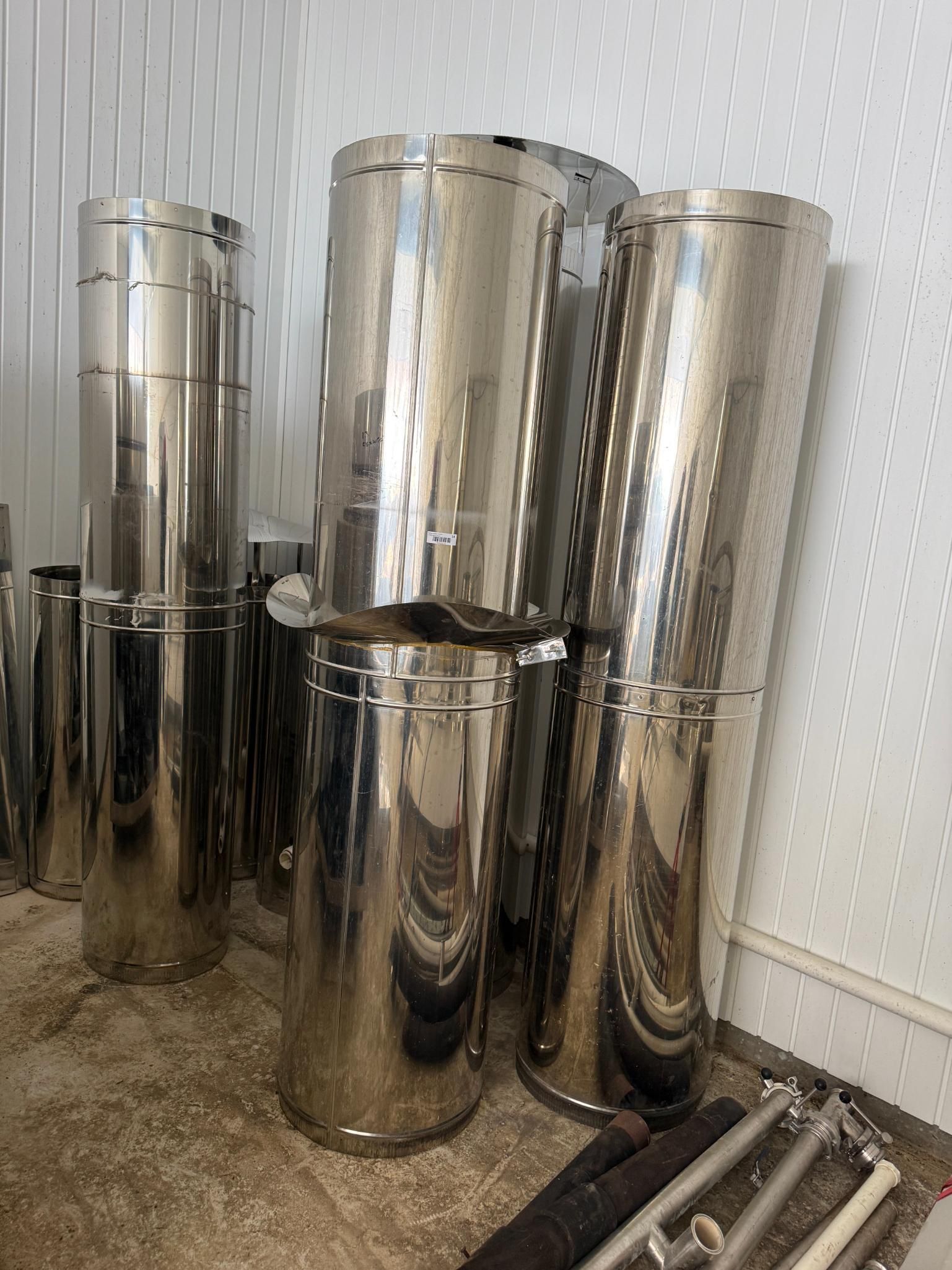 Stainless steel cylindrical containers stacked against a textured white wall.
