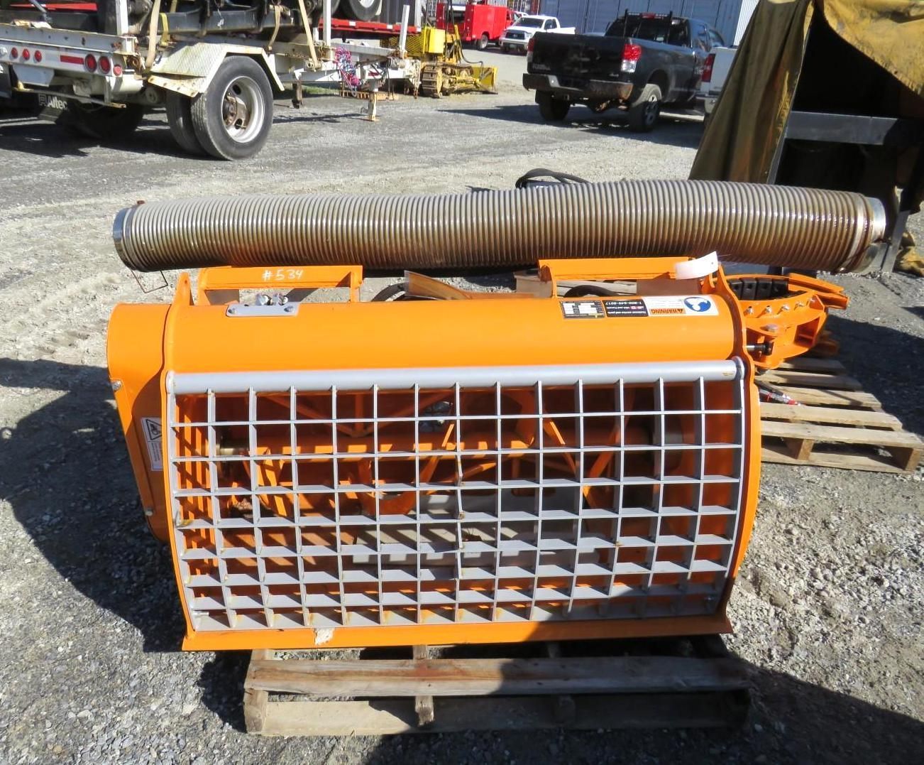 Orange concrete mixer with metal grid and hose, resting on a wooden pallet.