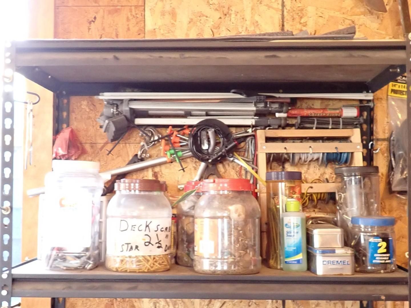 workshop shelf with jars, tools, wires, and containers against a wood-paneled wall