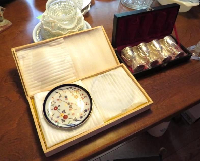 Wooden boxes holding a decorated plate and silver cups on a wooden table.