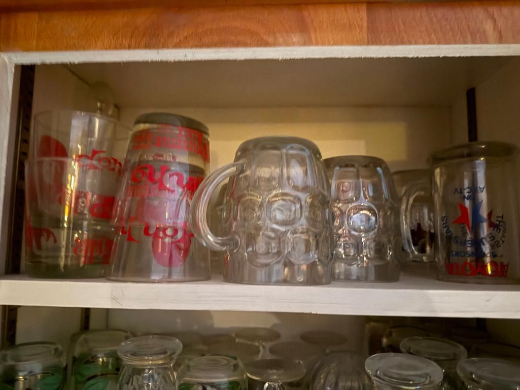 Glassware in a wooden cabinet, including beer steins and Coca-Cola glasses.
