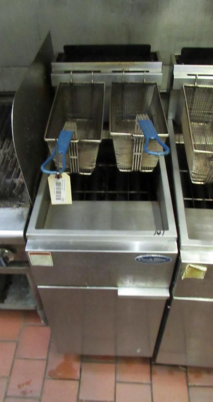 Stainless steel commercial fryer with two baskets and blue handles, in a kitchen setting.