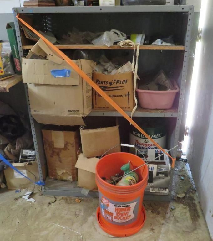 Metal shelving unit filled with boxes and items, secured by an orange strap.