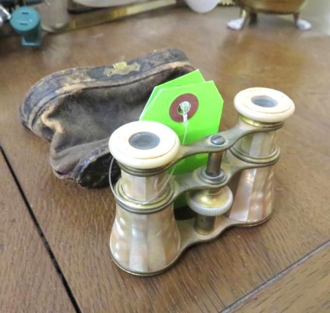 Antique opera glasses with mother-of-pearl accents and a leather case, on a wooden surface.