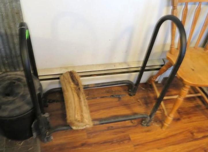 Black metal firewood rack on a wooden floor.