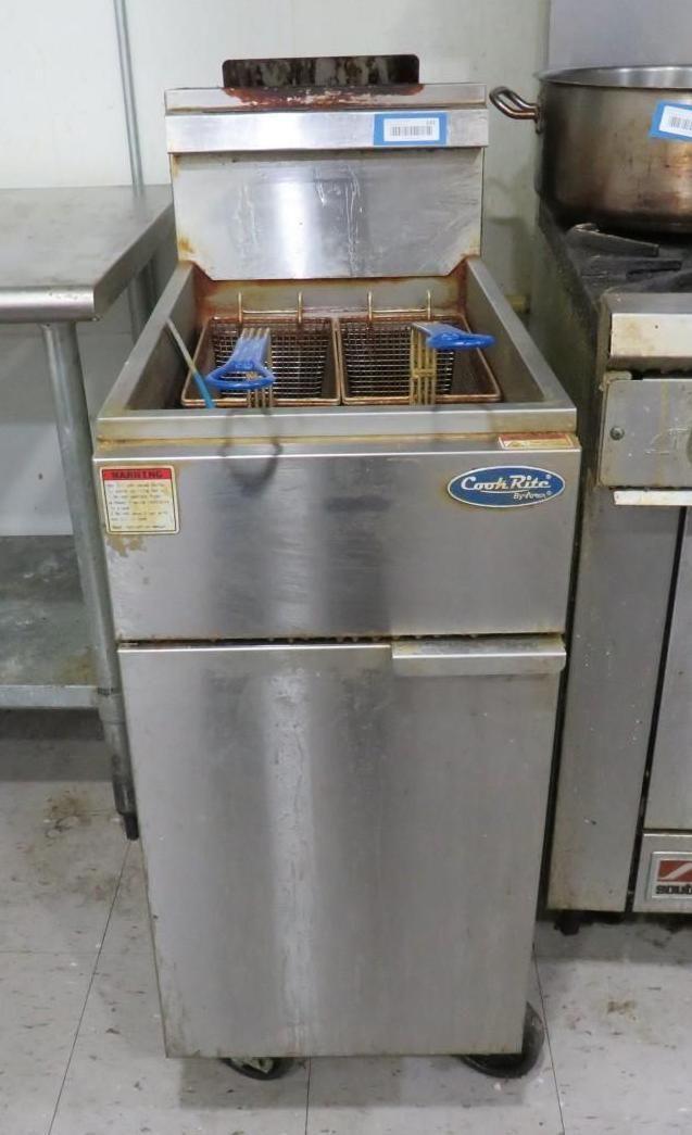 Commercial stainless steel deep fryer with fry baskets, a countertop, and a pot in a kitchen.