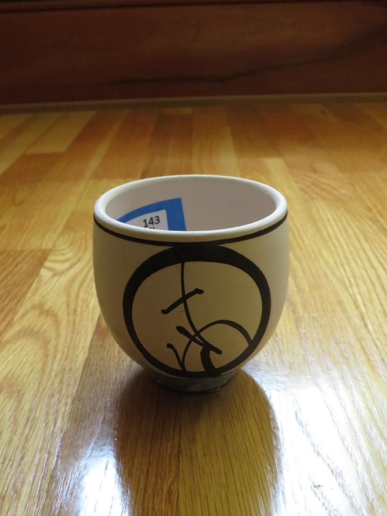 Cream-colored teacup with black calligraphy inside a black circle on a wooden floor.