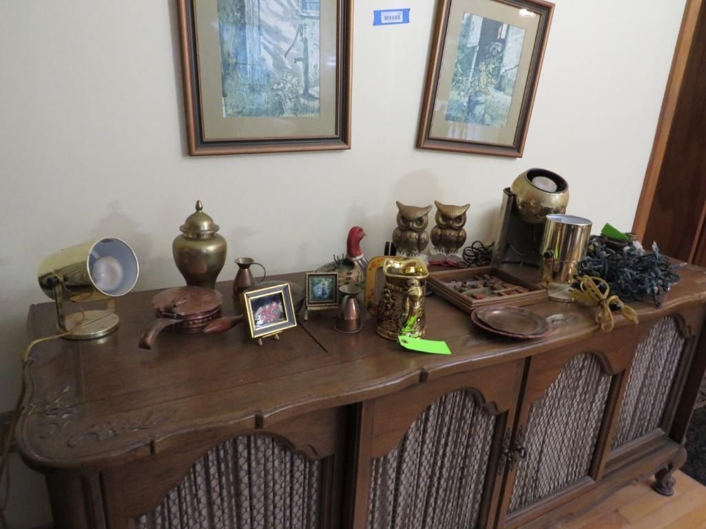 Wooden cabinet with decor including pictures, owls, and a lamp, beneath two framed landscape prints.