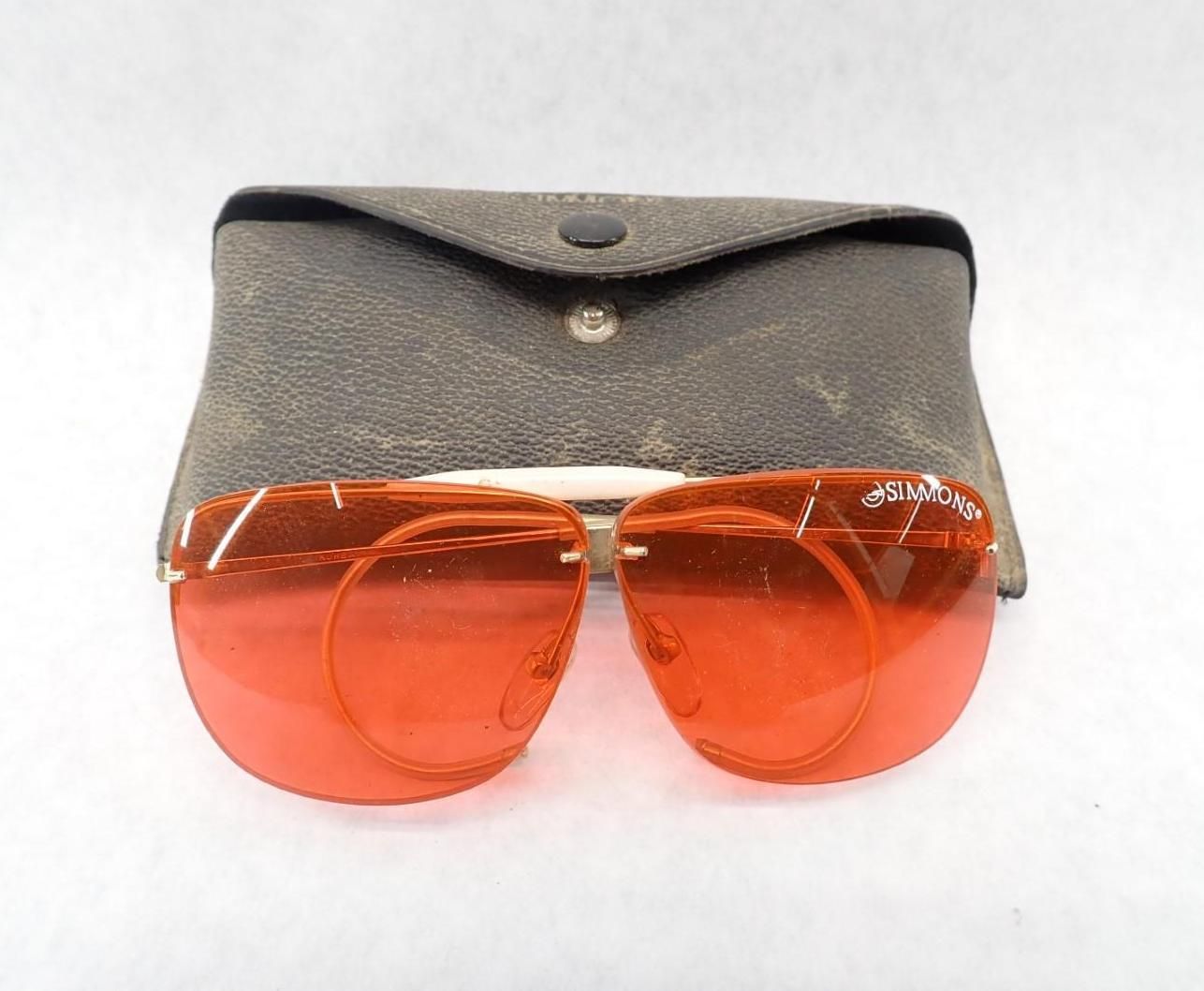 Rimless red lens sunglasses in front of a dark brown leather case.