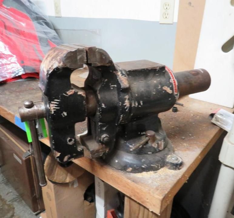 Black bench vise on a wooden workbench, with a red handle.