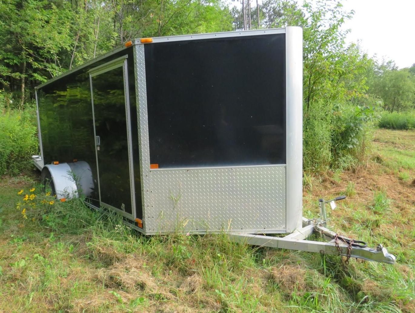 Black and silver enclosed cargo trailer parked on grassy ground.