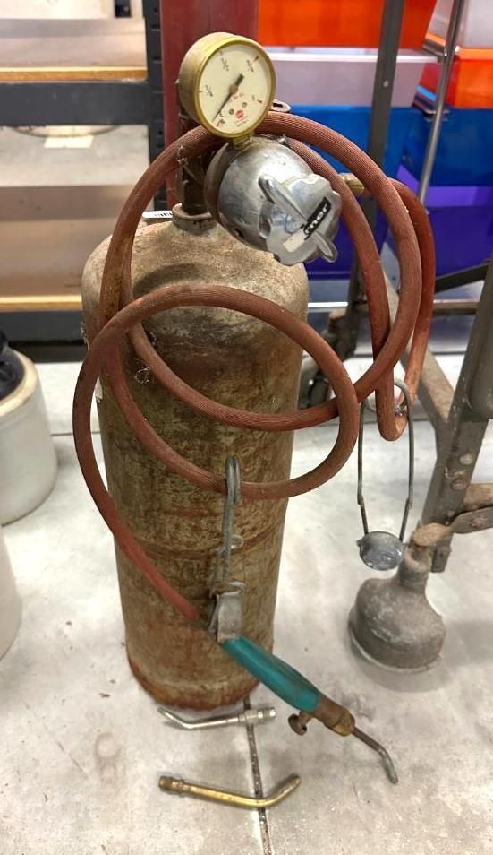 Metal oxygen tank with a pressure gauge, hose, and torch on a surface.