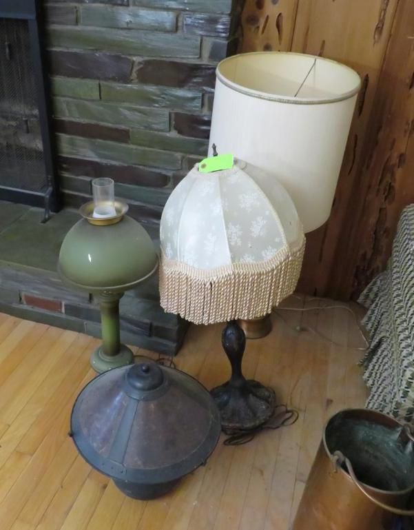 Four vintage lamps on a wooden floor, near a stone fireplace and wooden wall paneling.