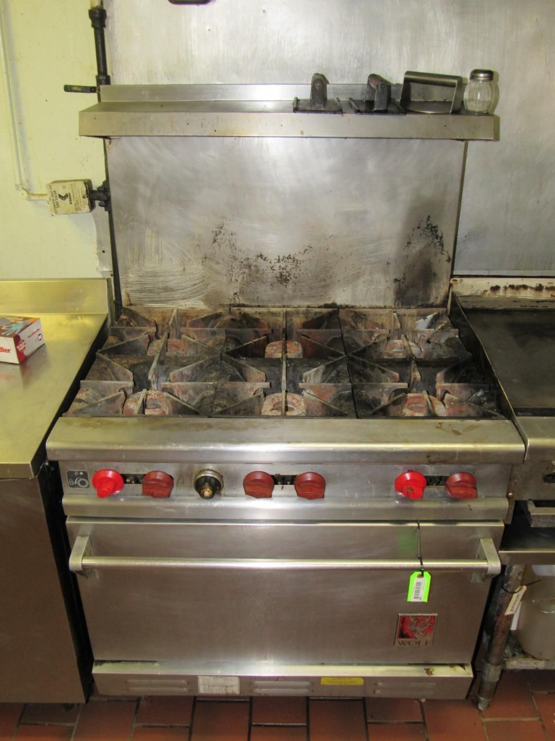 Commercial stainless steel gas range with four burners, control knobs, and a backsplash, in a kitchen.