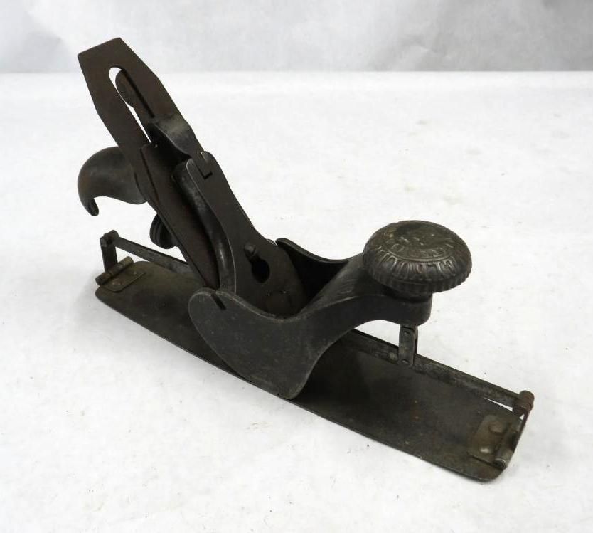 Small, dark metal block plane with a round knob and lever.
