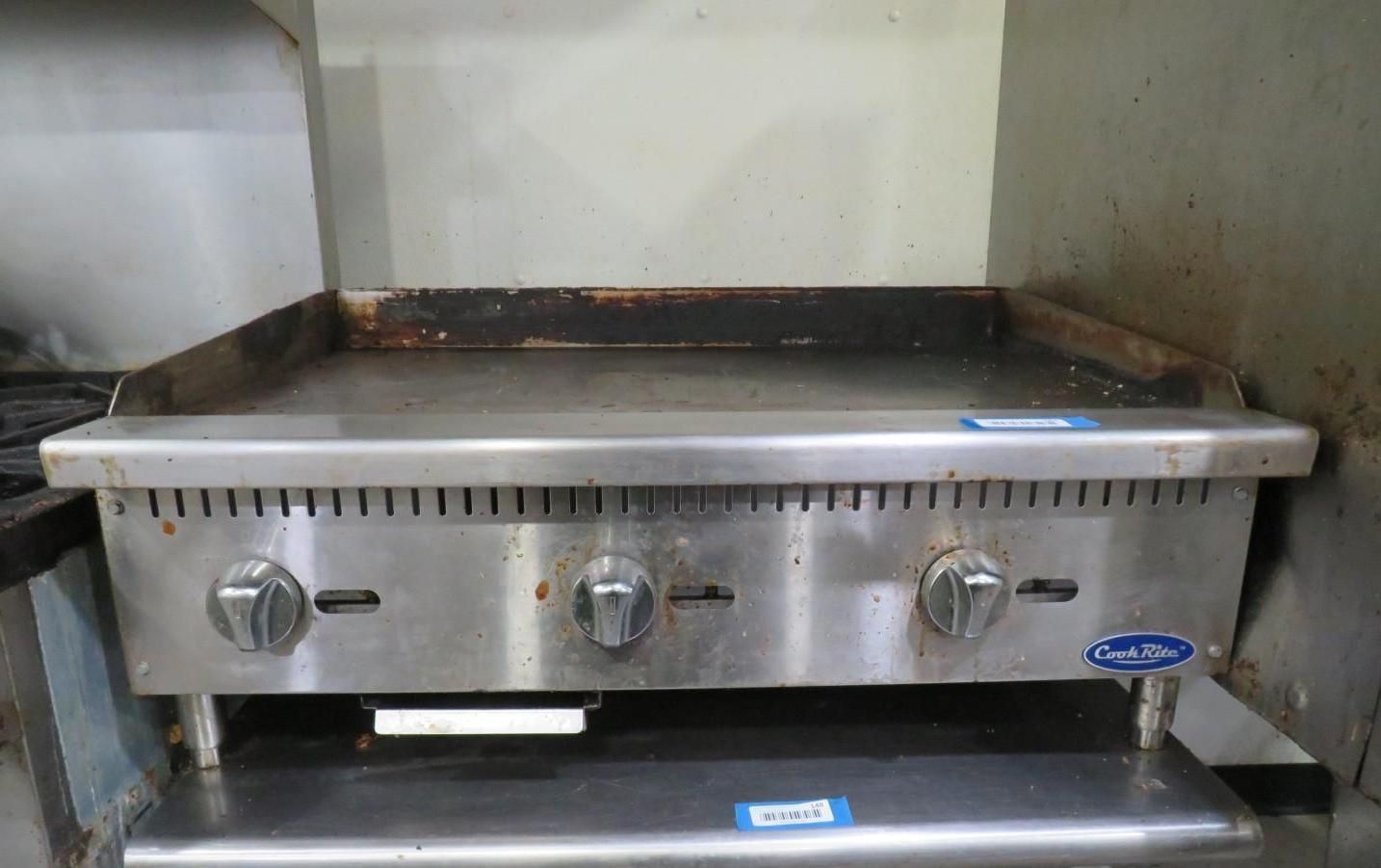 Stainless steel commercial flat-top griddle with three control knobs, in a kitchen.