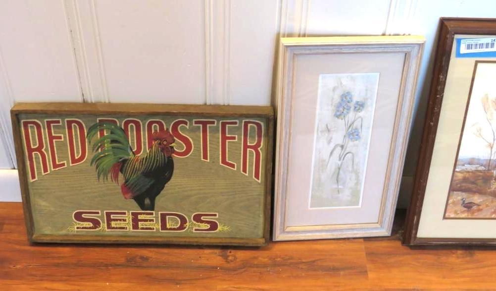 Red Rooster Seeds sign next to two framed pictures on a wooden floor.
