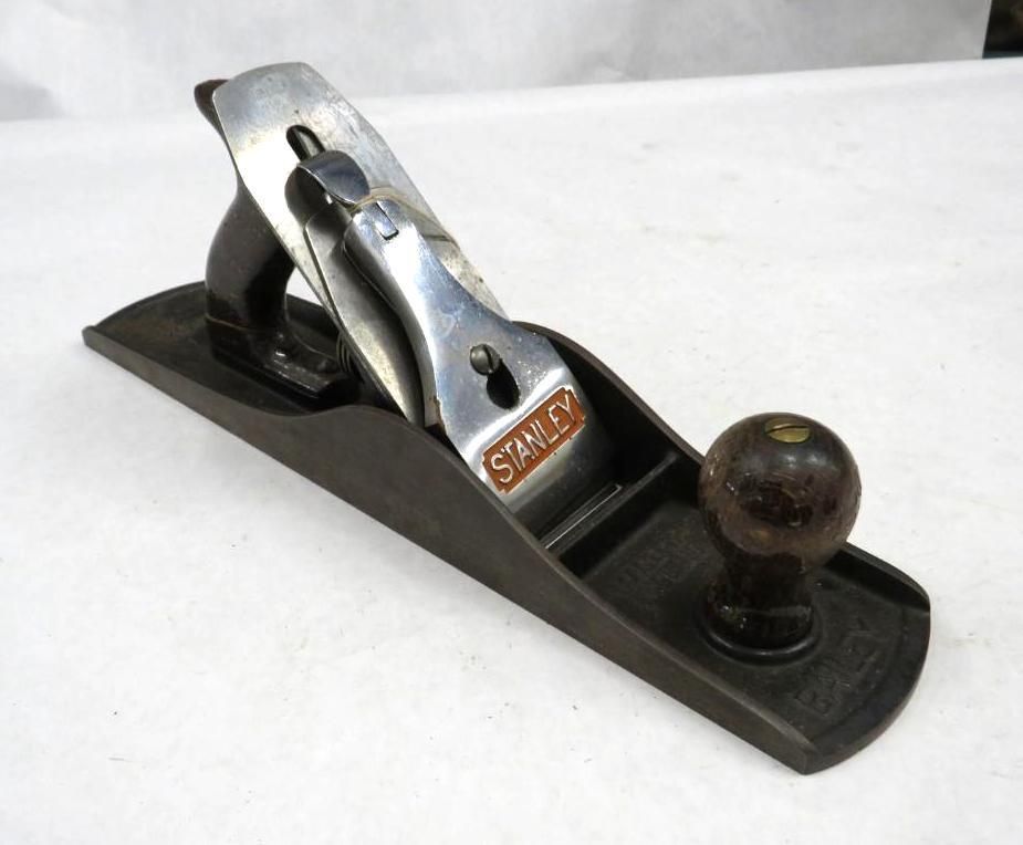 A vintage Stanley hand plane with a dark wooden body, metal blade, and handle on a white surface.