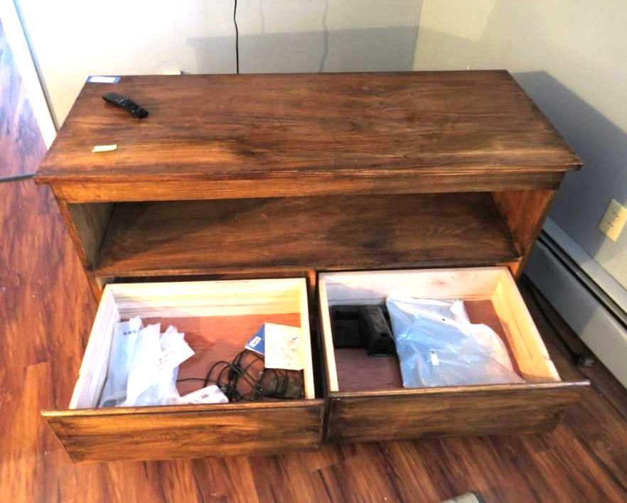 Wooden media console with two open drawers, displaying items on a wood floor.