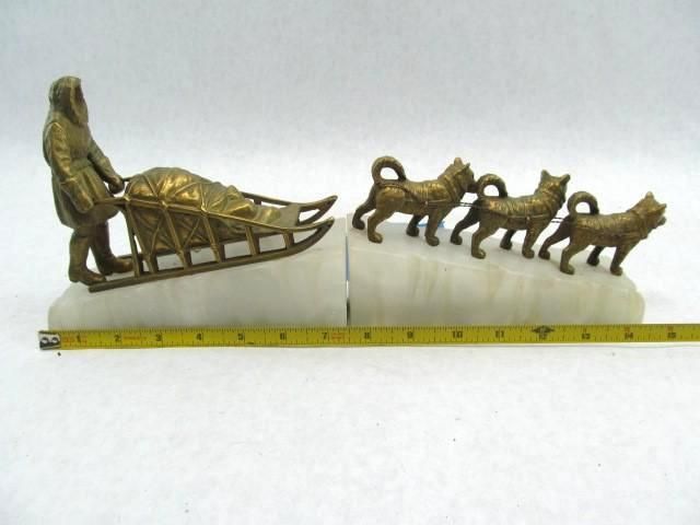 Bronze sled dogs and musher statue on a white onyx base, with a tape measure.