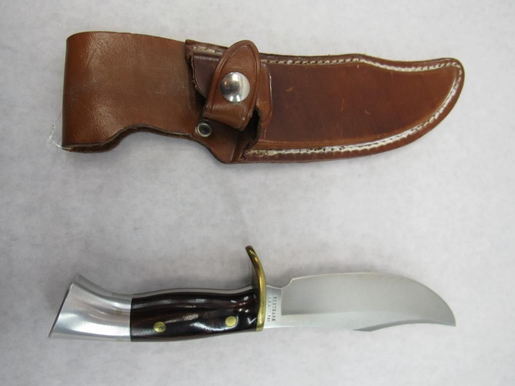 Knife with brown leather sheath; knife has black handle, silver metal accents, and curved blade.