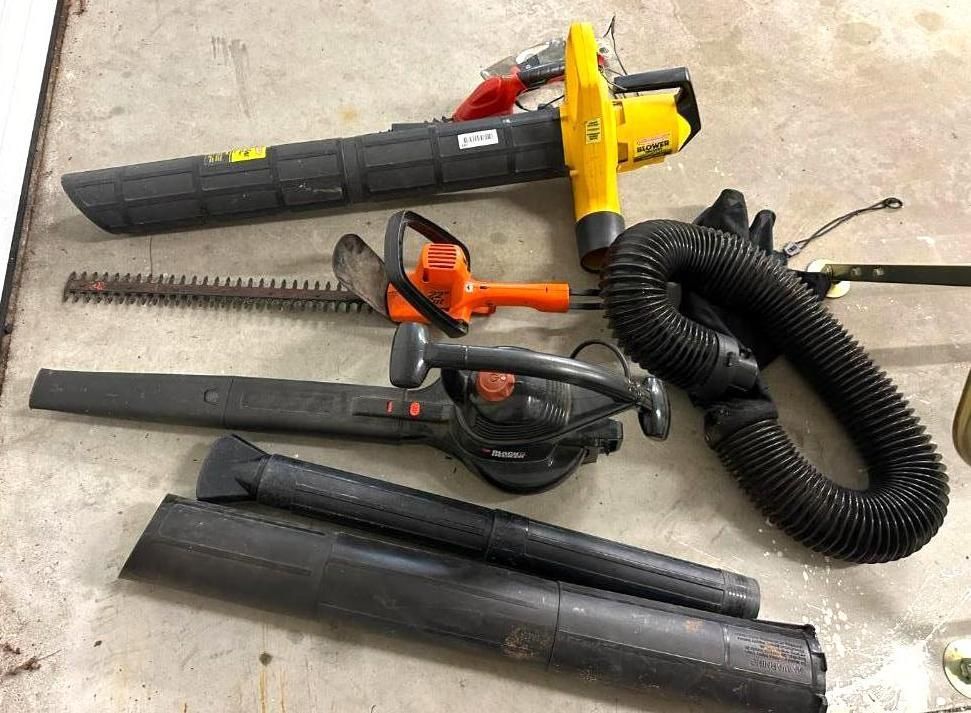 Lawn tools: yellow leaf blower, orange hedge trimmer, black vacuum, and extensions on a concrete surface.