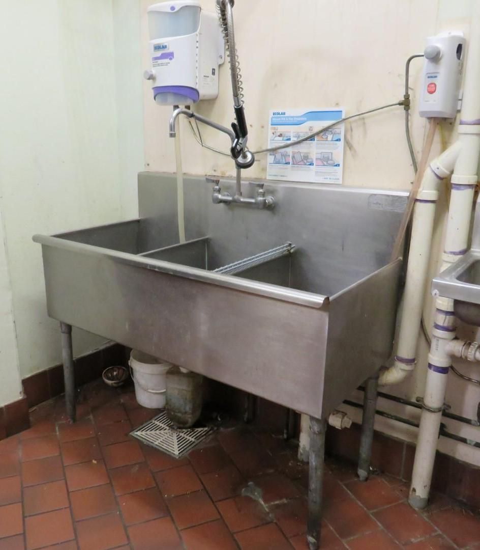 Stainless steel three-basin sink in a commercial kitchen with soap and drying dispensers.