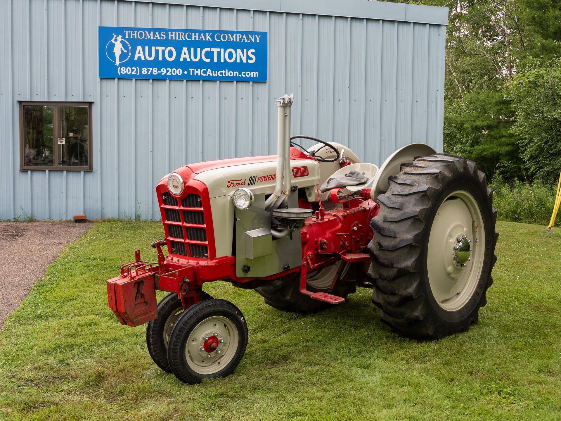 Red and gray Ford tractor in front of a blue building with an auto auction sign.