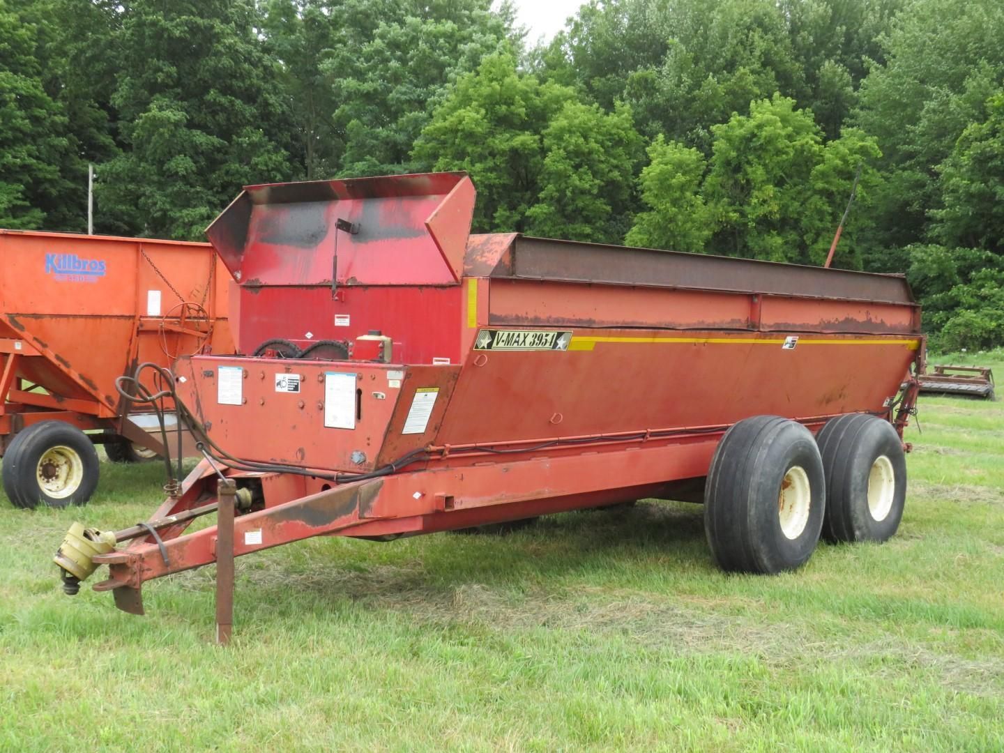 Red farm fertilizer spreader with dual wheels on grassy field.