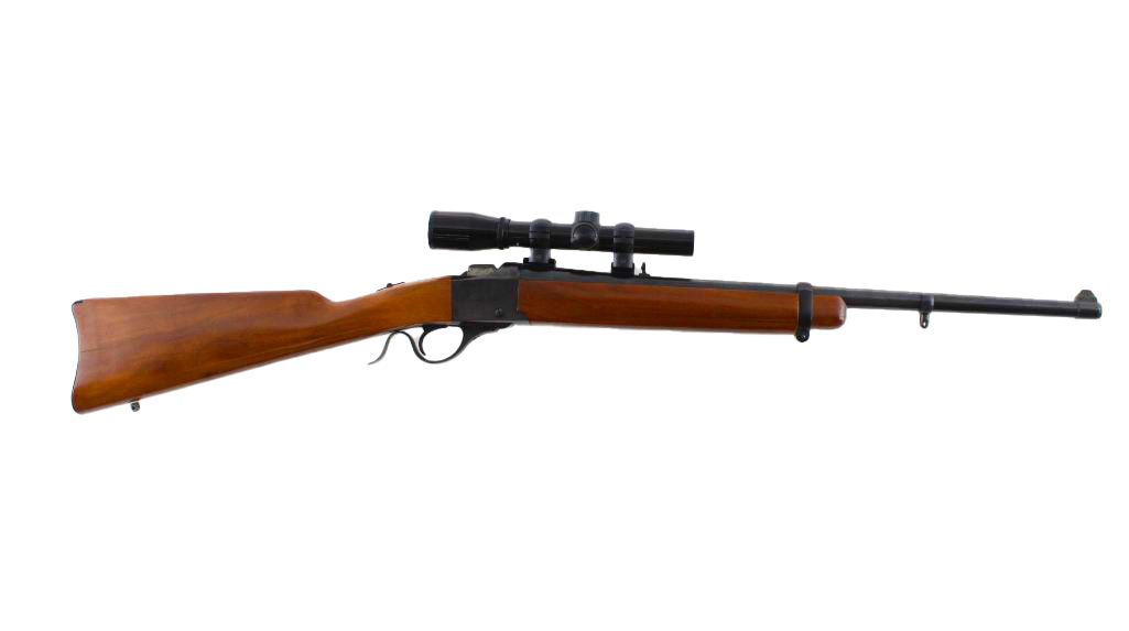 Rifle with wooden stock, scope, and black barrel, on a white background.