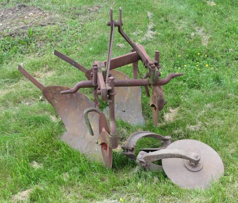 Rusty farm plow resting in green grass.
