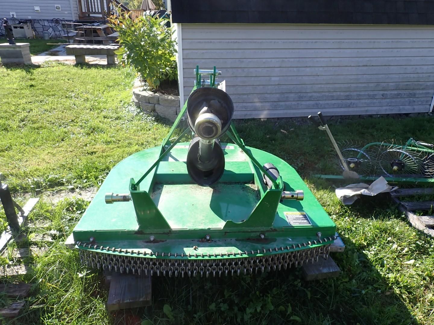 Green brush mower parked on grass beside a house, with a black chute centered on top.