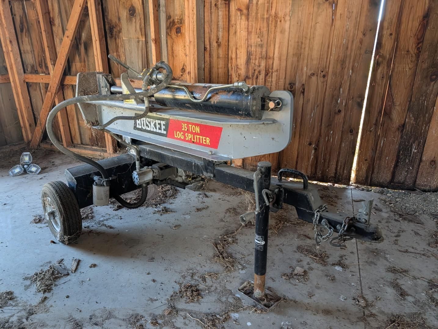 trailer-mounted log splitter in a barn, with a wooden fence in the background.