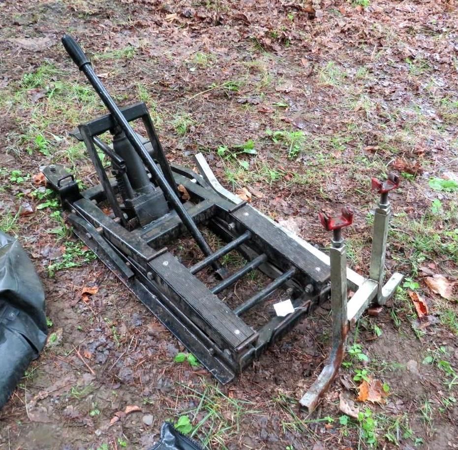 Black hydraulic lift on ground with two silver support stands.
