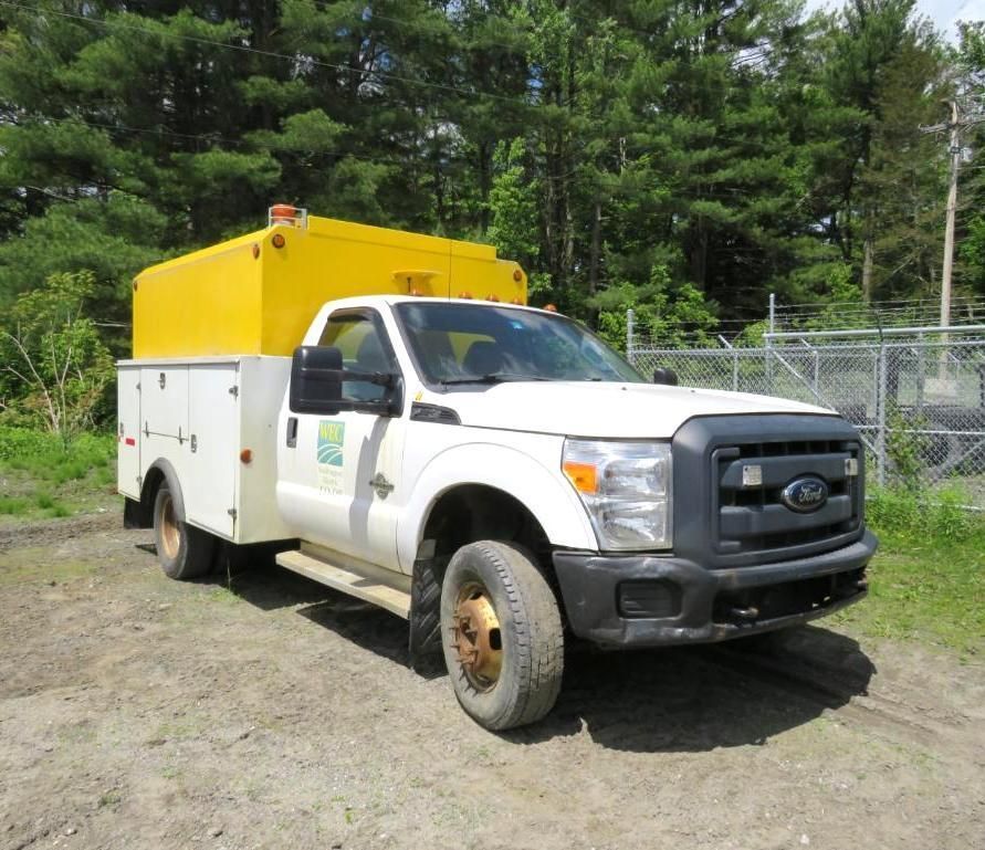 White Ford work truck with yellow top box parked on gravel.