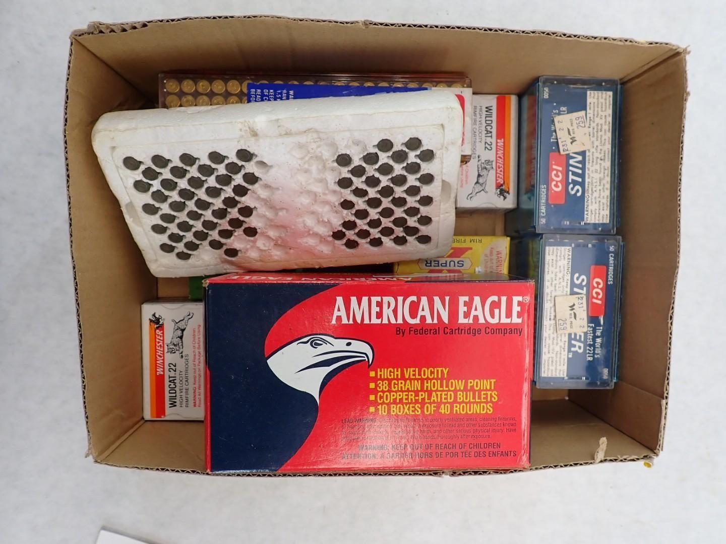 Cardboard box filled with boxes of ammunition. Includes American Eagle brand and others, various colors.