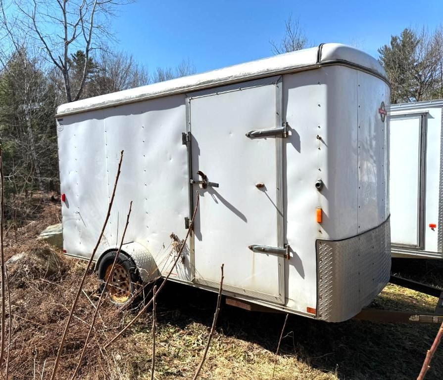 White cargo trailer with closed doors and wheels, parked outdoors.